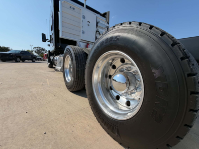 Kenworth T680 truck wheel and dual rear tires with polished hubcap and rugged tire tread; side cab area visible in background.