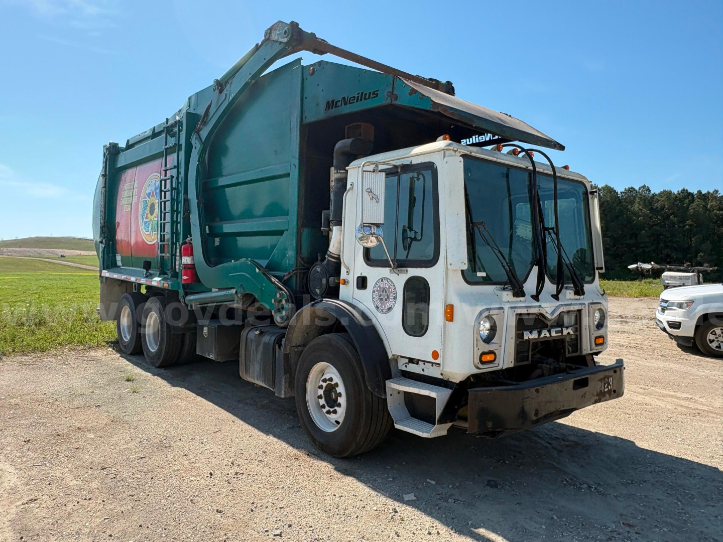 Garbage truck with white cab and green dump body, Mack MRU613, visible branding on front grille and side art, VIN and stock number not legible in image.