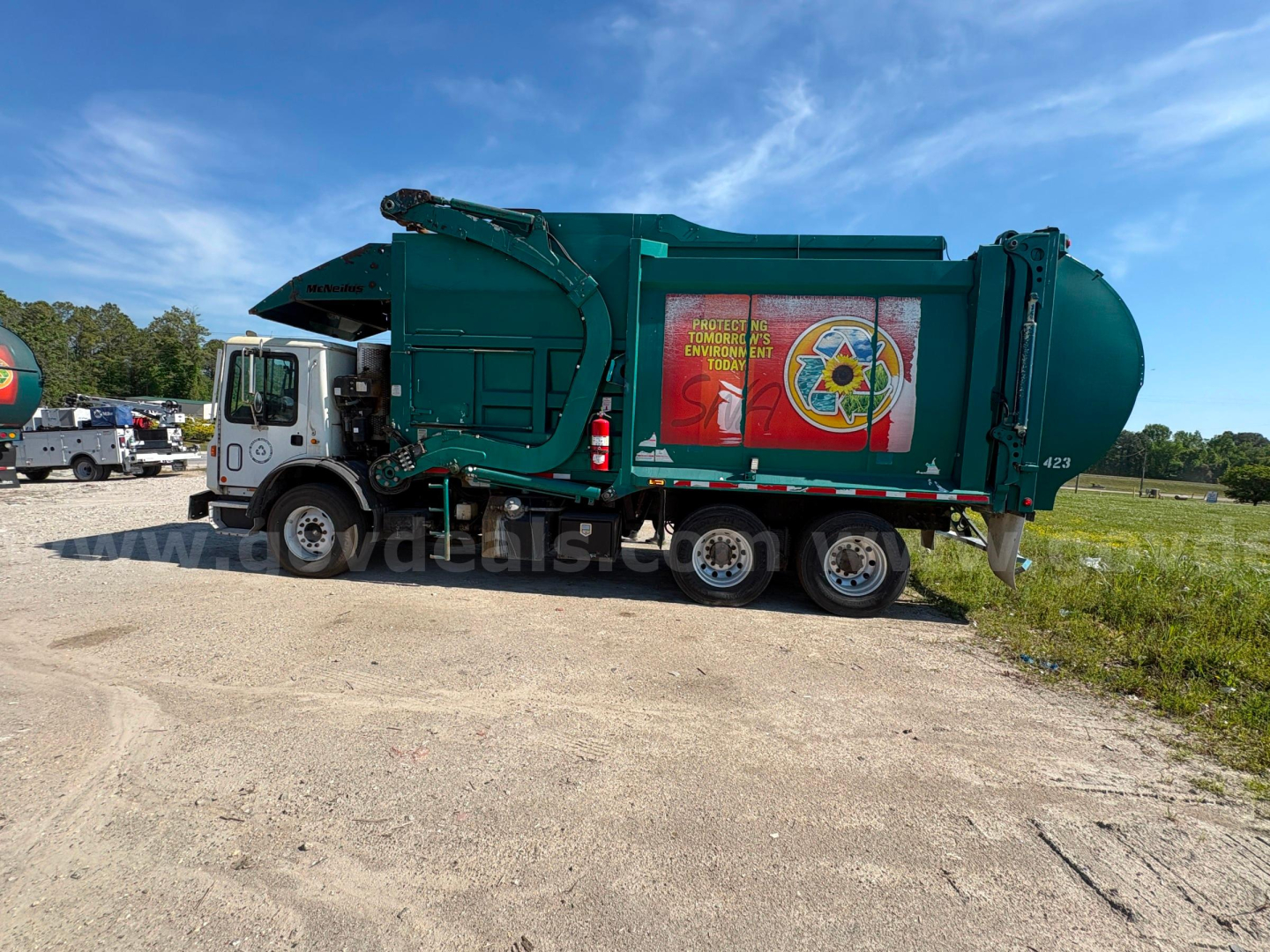 Garbage truck side view with green body and rear compactor, company logo on side, Mack MRU613 style with multiple wheels; no detailed readable labels.