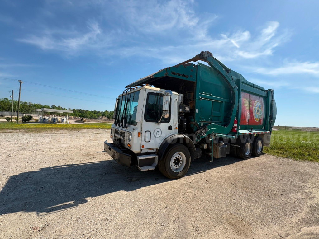 Garbage truck (Mack MRU613) in-service view showing cab and green refuse body with hydraulic arms.