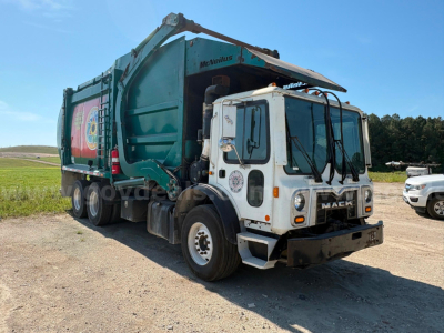 Garbage truck with white cab and green dump body, Mack MRU613, visible branding on front grille and side art, VIN and stock number not legible in image.