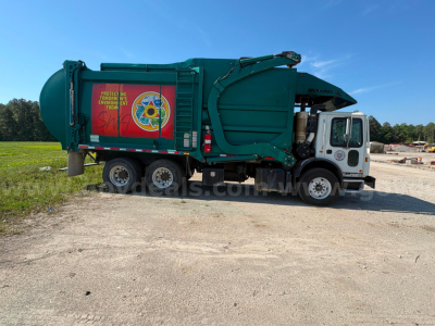 Garbage truck 2013 Mack MRU613 side view showing rear refuse body, green color, side graphics, and cab with white front.