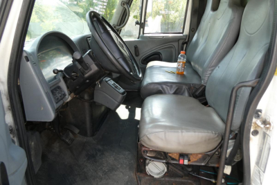 Interior cab of a 2004 International 4300 beverage truck showing gray fabric seats, steering wheel, dashboard, and a bottle on the passenger seat.