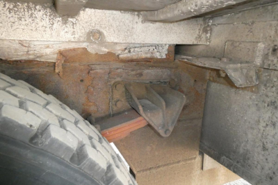 Underbody view of a 2004 International 4300 showing a rusted frame area, spare tire and leaf spring with an orange brake hose/line and mounting bracket.