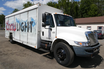 Truck side view showing International 4300 beverage truck with Cross Light graphic on white box; front shows grille and cab; visible text includes 'Cross LIGHT' on side, 'IH' style logo on door, and numbers on cab edge.