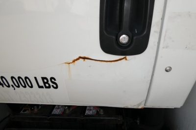 Truck side panel showing damaged white exterior with rust streak near a black handle and partial '0,000 LBS' text.
