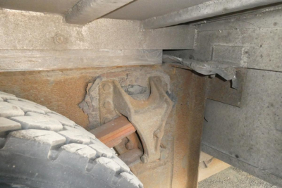 Truck frame underside showing suspension component and leaf spring, view near wheel well.