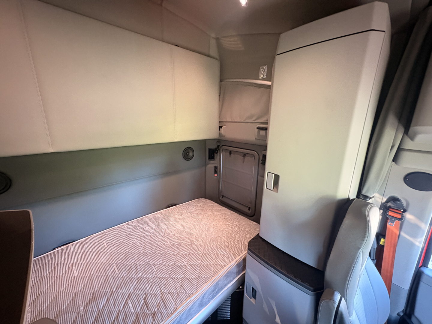 Kenworth T680 sleeper cab interior with bunk bed and cabinet, showing storage panels and seating area.