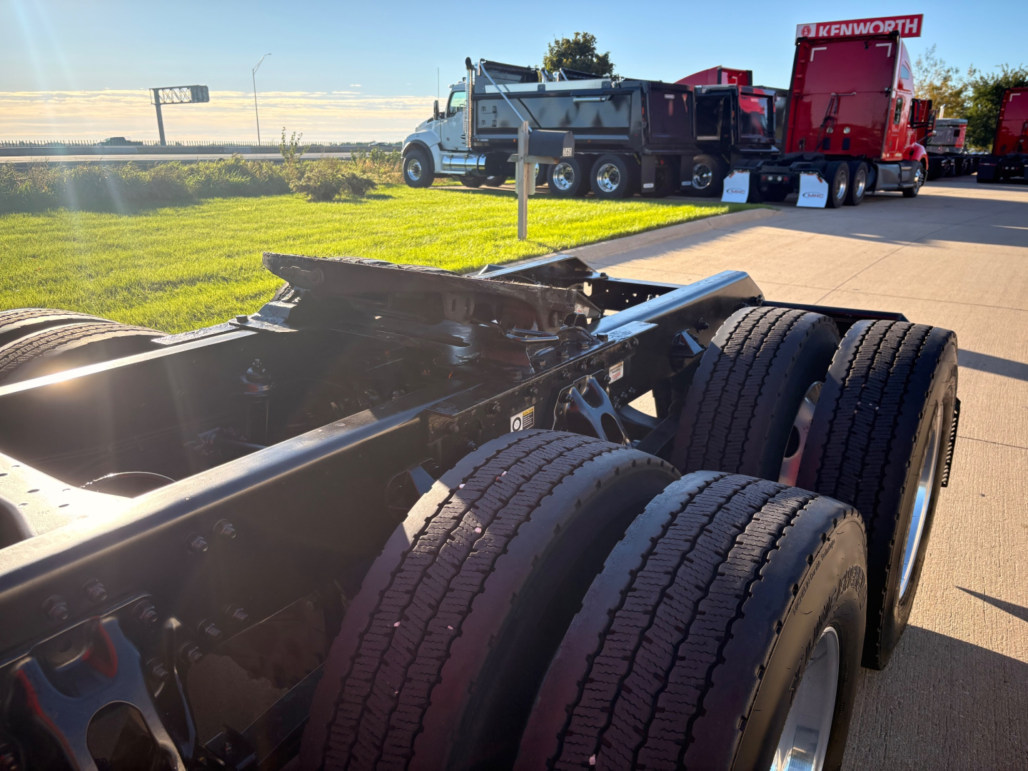 Kenworth T680 truck chassis and dual rear axles in foreground with other trucks in background at dealership.