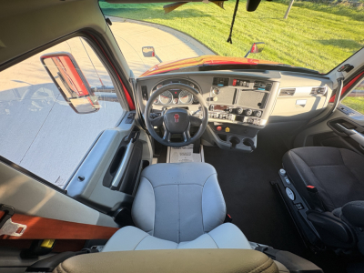 Kenworth T680 cab interior showing steering wheel dashboard and driver's seat with light gray upholstery.