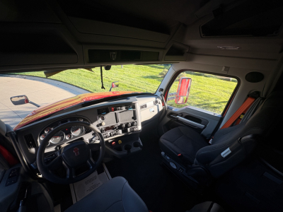 Cab interior of a 2022 Kenworth T680 tractor showing steering wheel, dashboard, and passenger seat with controls.