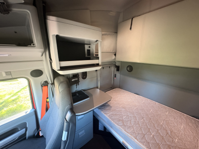 Truck sleeper cabin interior with bunk bed and overhead cabinet; small microwave shelf visible and cup holder area.