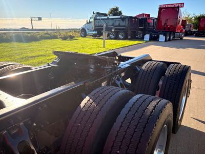 Kenworth T680 truck chassis and dual rear axles in foreground with other trucks in background at dealership.