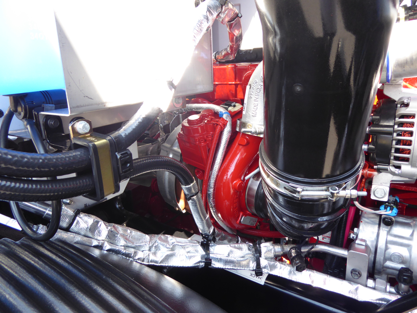 Engine bay showing red turbocharger and black intake pipe, metal braided lines, hoses, and various engine components.