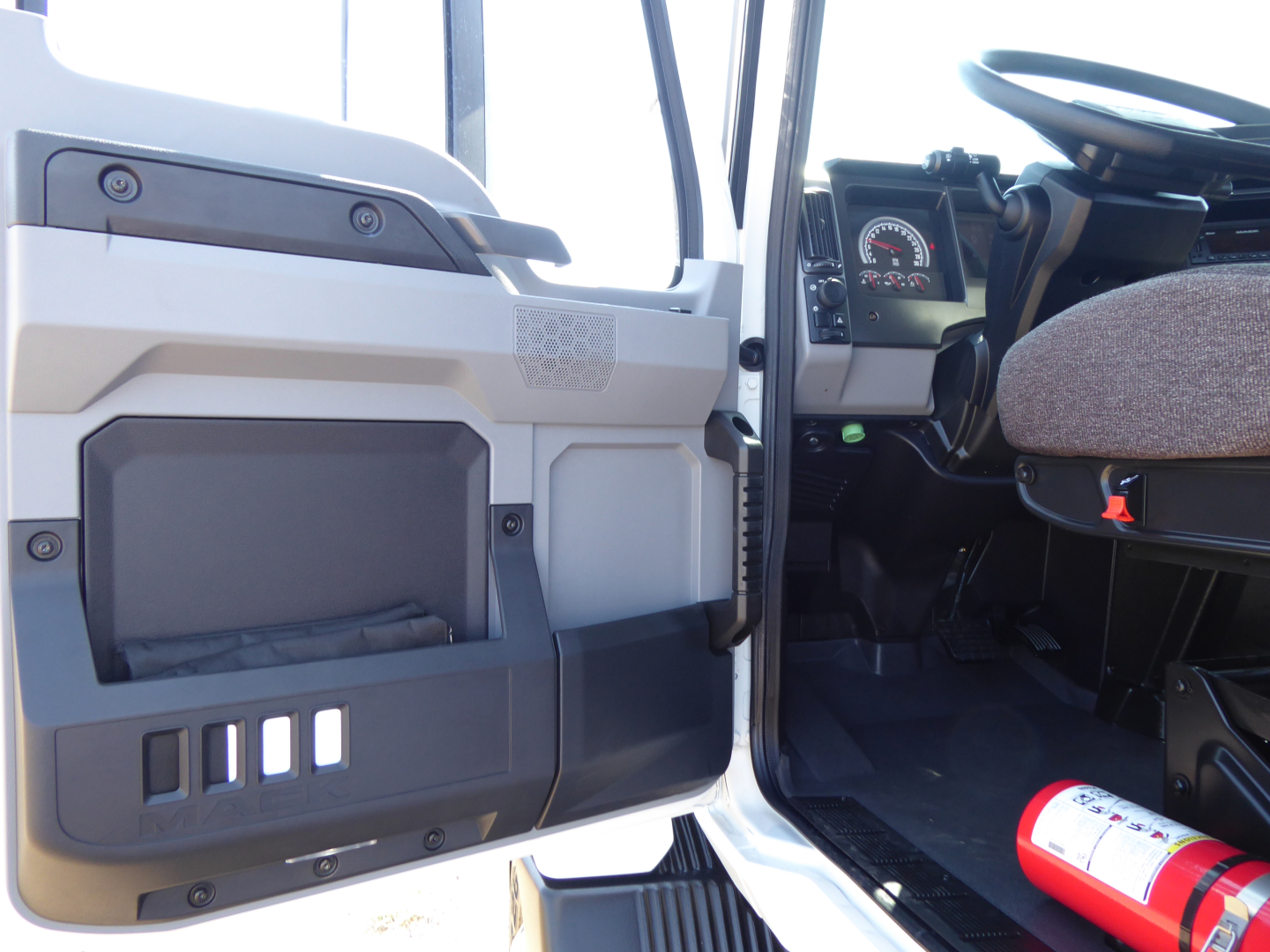 Truck cab interior of a 2025 Mack MD6 with open driver door showing dashboard and steering wheel, VIN tag and stock number visible.