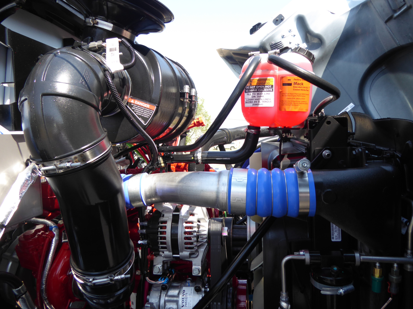 Mack MD6 engine bay showing air intake ductwork, red reservoir, blue accordion hose, and various hoses and cables.