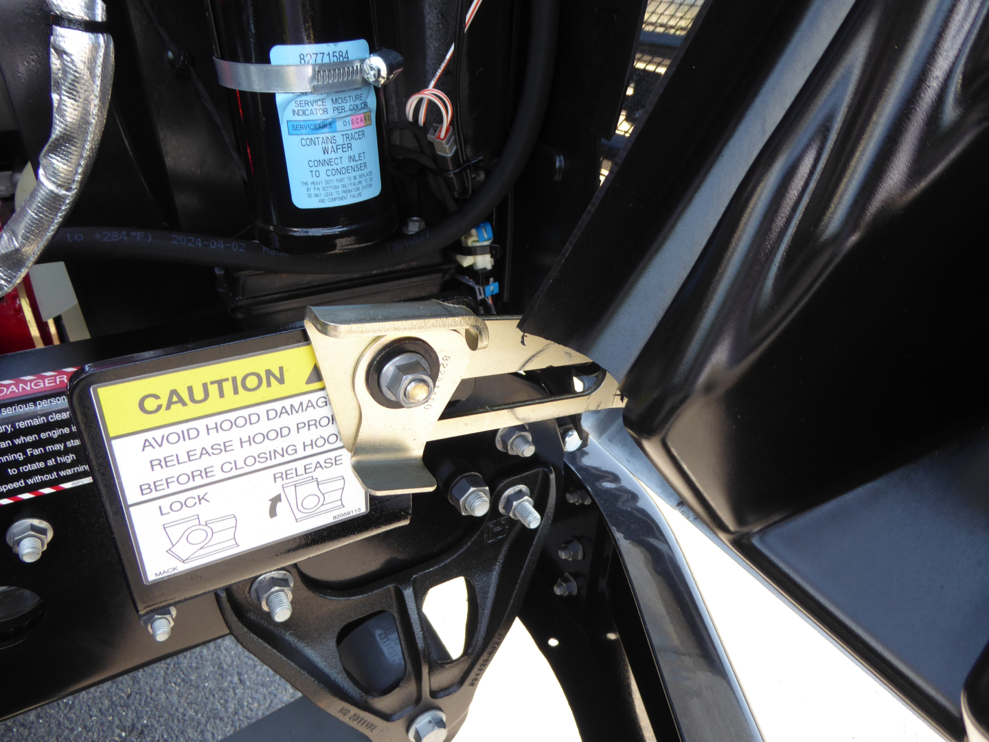 Mack MD6 engine bay area showing caution label, hydraulic hose, and blue filter near black metal framework.
