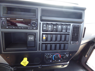Dashboard of a Mack MD6 truck showing radio with 'MACK' branding, multiple toggle switches, climate controls, and a yellow 'PARKING BRAKE' knob.