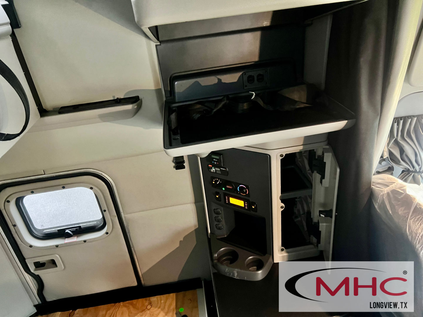 Peterbilt truck interior showing a control panel with power outlets, switches, and a small open compartment; MHC Longview logo bottom-right.