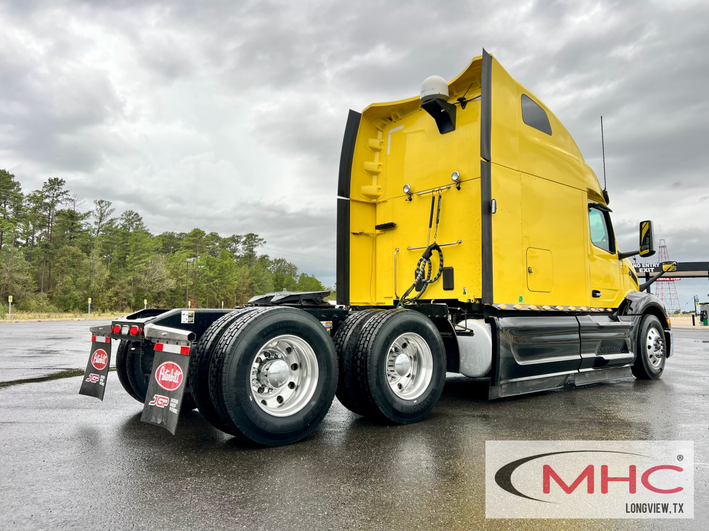 Peterbilt 579 truck with yellow cab seen from rear three-quarter view. Dual rear axles, mudflaps with red logos, black side skirts, overcast sky.