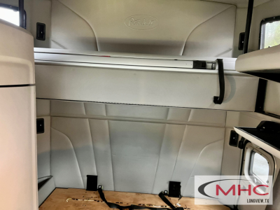 Peterbilt truck cab interior storage area with upper bunk/console and silver panels, logo embossed, light gray upholstery; MHC Longview watermark.