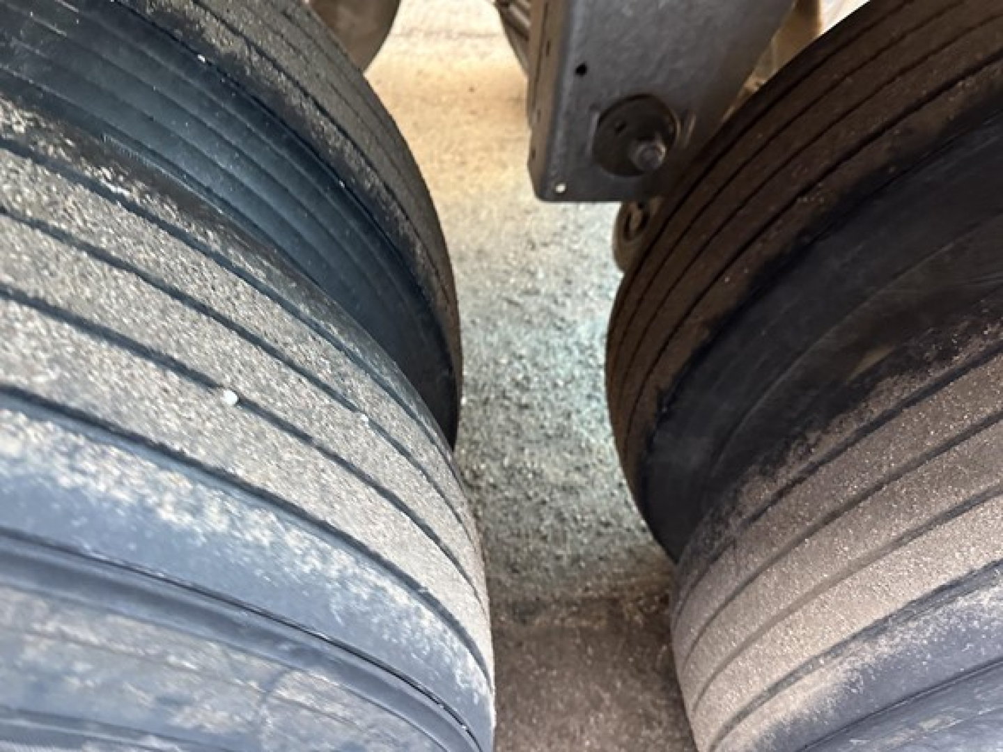 Trailer tires and suspension view showing dual axles on a Stoughton grain trailer with wheel rims and gravel surface.