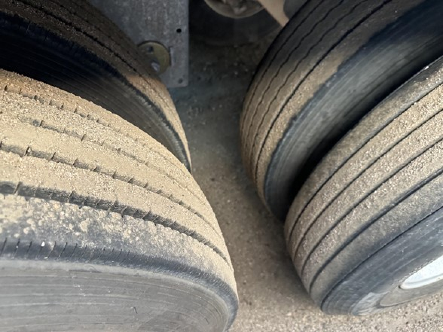 Trailer dual-tire assembly view showing treaded tires with dirt and grime, part of a Stoughton grain trailer axle setup.