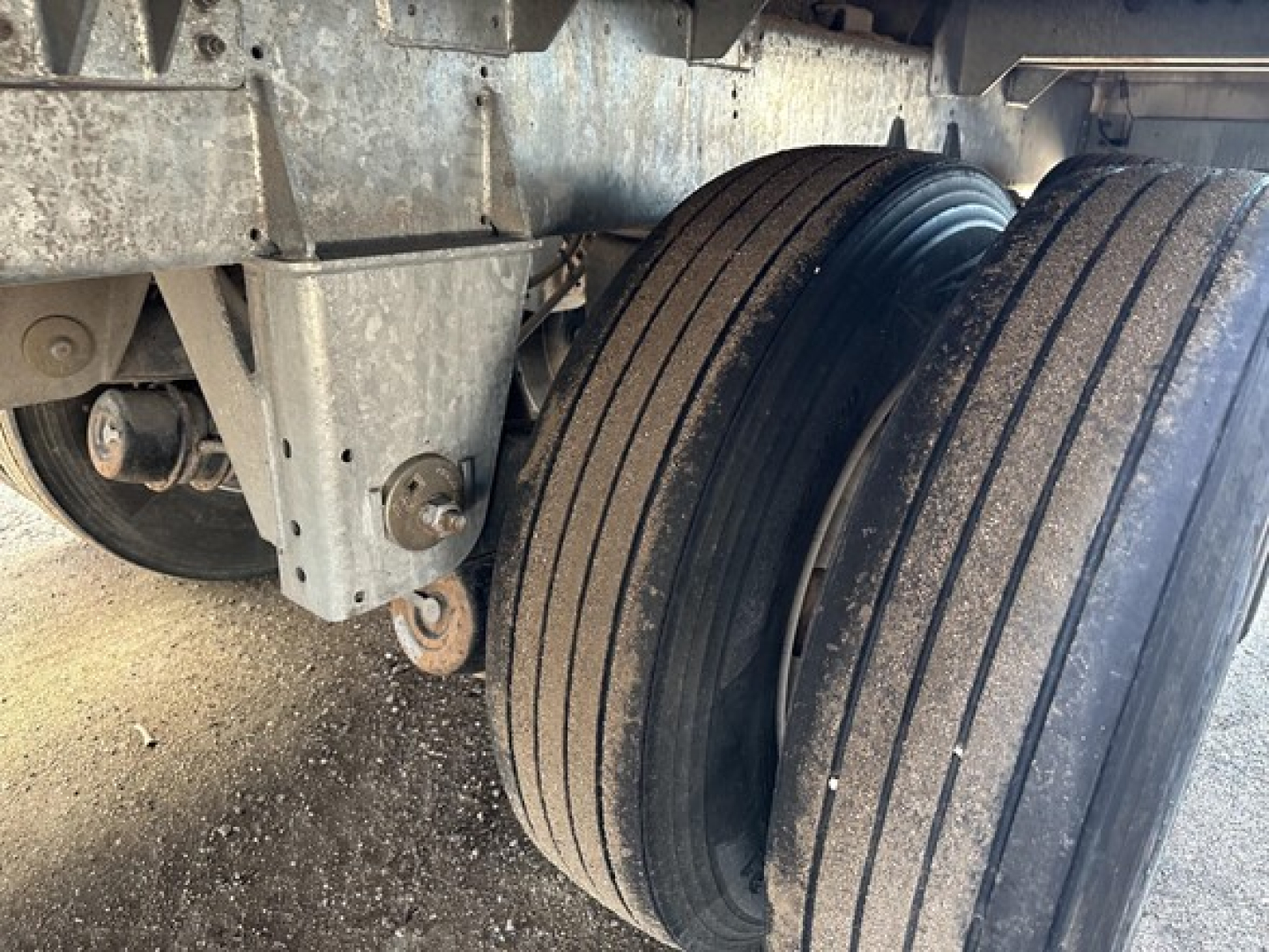 Trailer wheel assembly showing dual rear tandem axles with rims and tire tread patterns; metallic frame and suspension components visible.