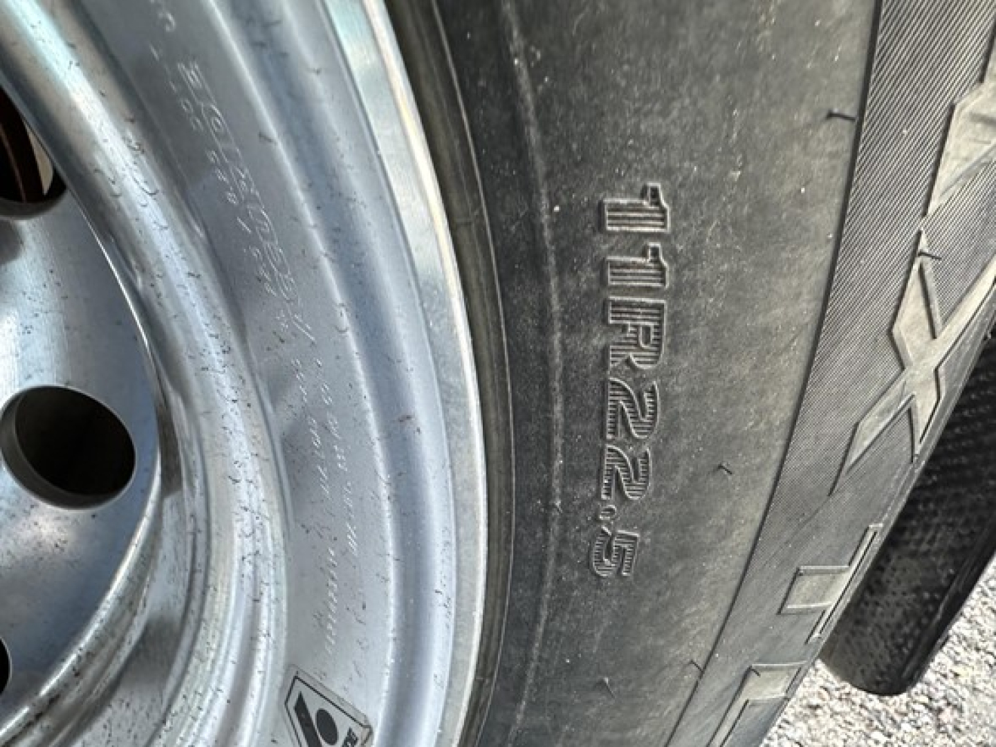 Trailer tire and wheel with embossed tire size 11R22.5/AXLE on sidewall; rim metallic with some dirt.