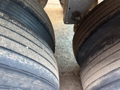 Trailer tires and suspension view showing dual axles on a Stoughton grain trailer with wheel rims and gravel surface.