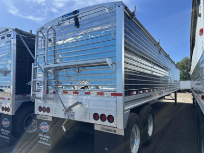 Stoughton grain trailer in a trailer yard showing side rails, rear barn doors, and dual rear axles with round taillights; chrome finish and ramps; visible VIN sticker area.