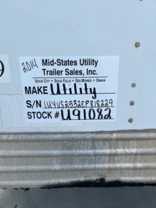 Sticker on trailer showing Make Utility label with S/N and Stock number. Text reads: 2014 Mid-States Utility Trailer Sales, Inc. Sioux City Sioux Falls Des Moines Omaha MAKE UTILITY S/N 1UYVS2532EP818229 STOCK # U91082.