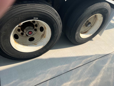 Dual rear trailer wheels with white rims and black tires; visible tire treads and wheel hubs, some corrosion around lug nuts.