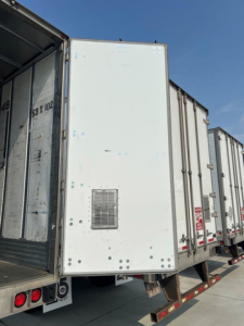 Trailer end and side doors of a white utility van trailer showing vent panel and reflective markings.