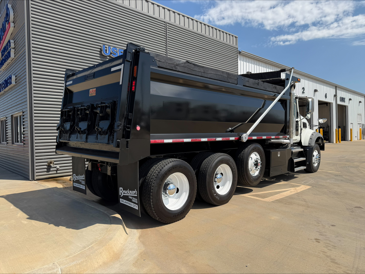 Dump truck: 2023 Mack GR84F dump truck in side-rear view showing dump bed, dual rear axles, white cab, black cargo bed, and safety rails.