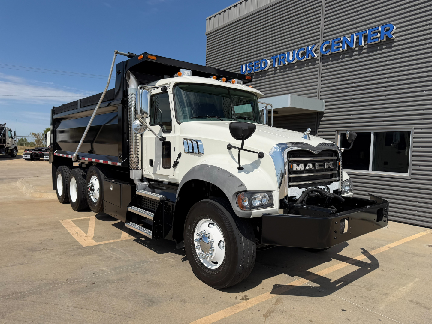 D8 Mack GR84F dump truck showing front view with chrome grille, large black bumper, and dump bed in a dealership lot.