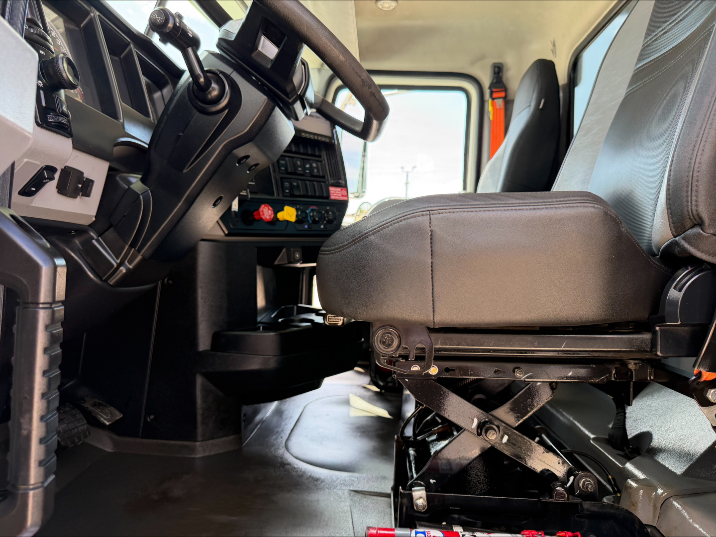 Interior of a 2023 Mack GR84F cab showing the driver's seat, steering wheel, control panel, and dash area; visible are switches and levers near the center console.