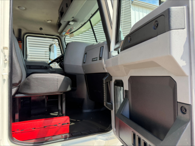 Truck cab interior of a 2023 Mack GR84F showing the driver seat, dashboard, and open passenger door with storage compartments.