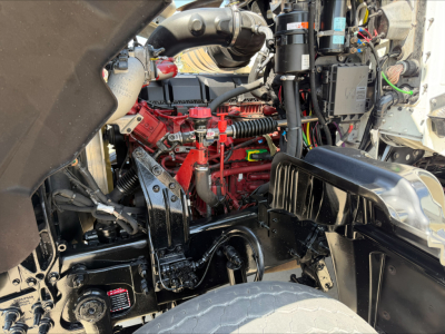 Mack GR84F engine bay showing red engine block, black air intake, hoses, and electrical wiring under hood.