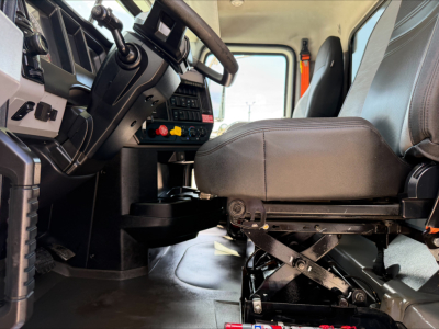 Interior of a 2023 Mack GR84F cab showing the driver's seat, steering wheel, control panel, and dash area; visible are switches and levers near the center console.