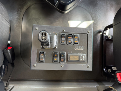 Panel with multiple switches, a circular socket, and a digital readout mounted inside a Mack GR84F dump truck cab area.