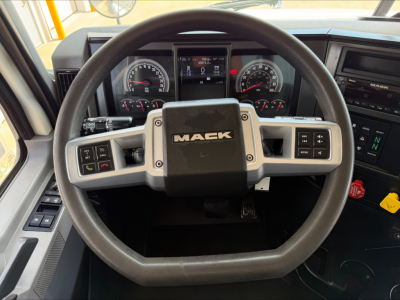 Steering wheel and instrument cluster of a Mack GR64 or GR84F truck cab with Mack logo on the center of the steering wheel. Instrument gauges visible behind, center display, and controls on the steering wheel.