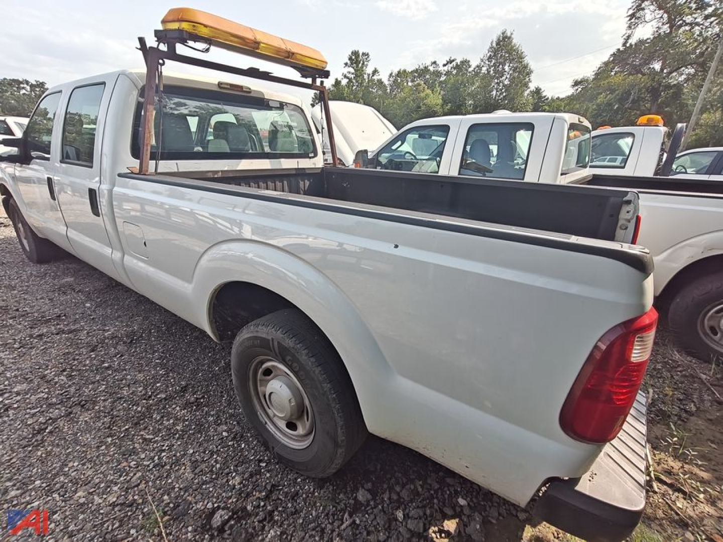 Ford F-250 Super Duty crew cab pickup truck side/rear view showing long bed, white paint, orange rooftop beacon, and utility rack.