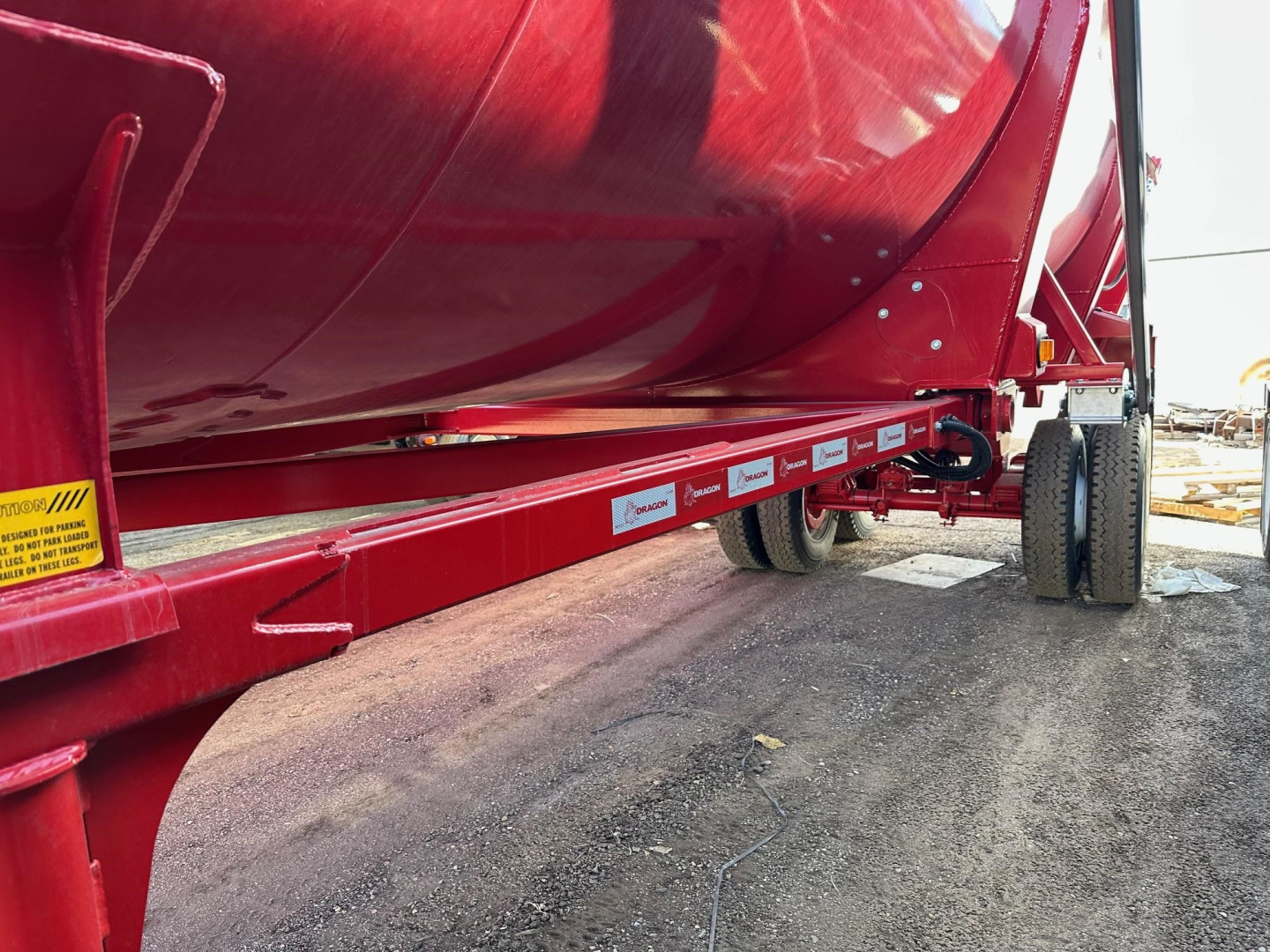 Dump trailer with red chassis showing side labels and wheels in view.