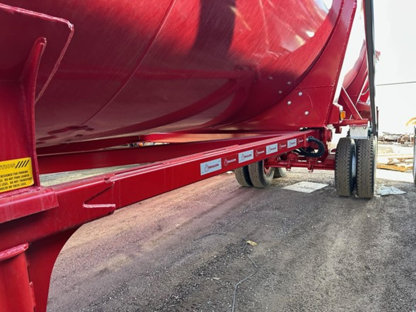 Trailer side view of a red Ranco rock end dump with long flatbed rail, labels along the side, and dual rear wheels in an outdoor yard.