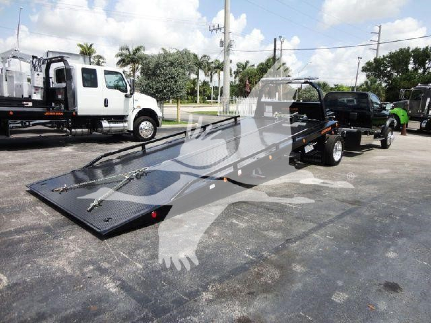 Ram 5500 rollback tow truck with a long low-profile flatbed and a black metallic finish, dual rear wheels, and a white cab in background.