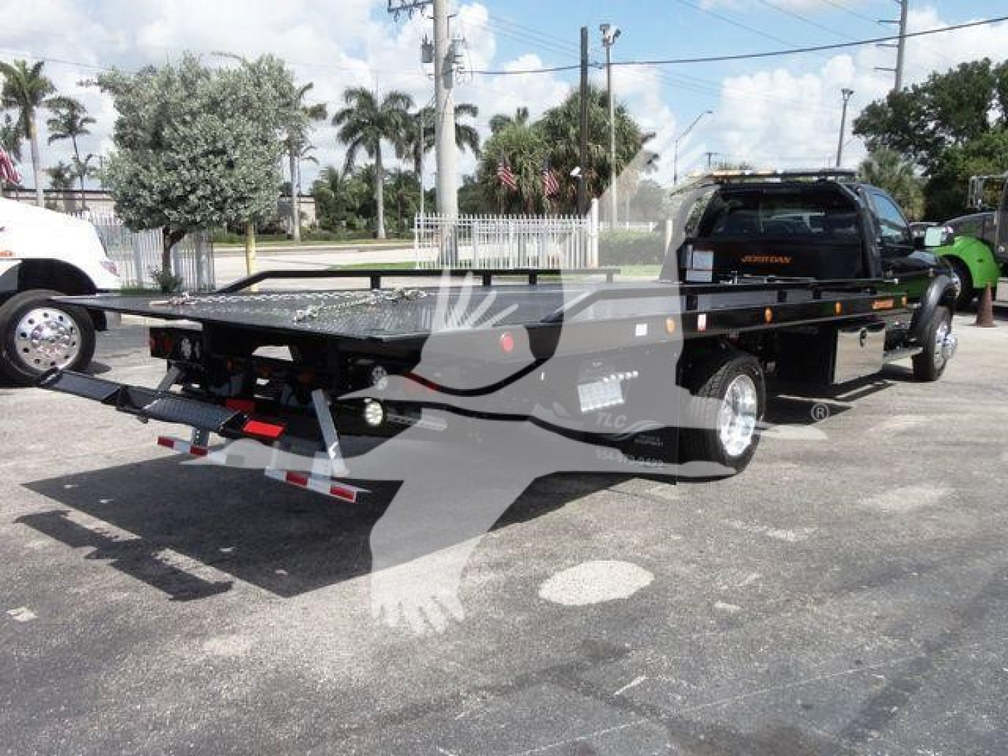 Ram 5500 rollback truck with flatbed seen from rear-left quarter, black flatbed, trailer-mounted equipment, rear lights visible.