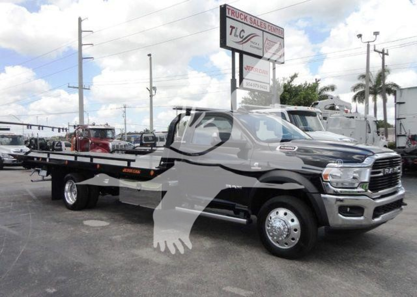 Ram 5500 tow truck/rollback with flatbed, chrome grille, dual rear wheels, and large side mirrors; truck dealership lot in background.