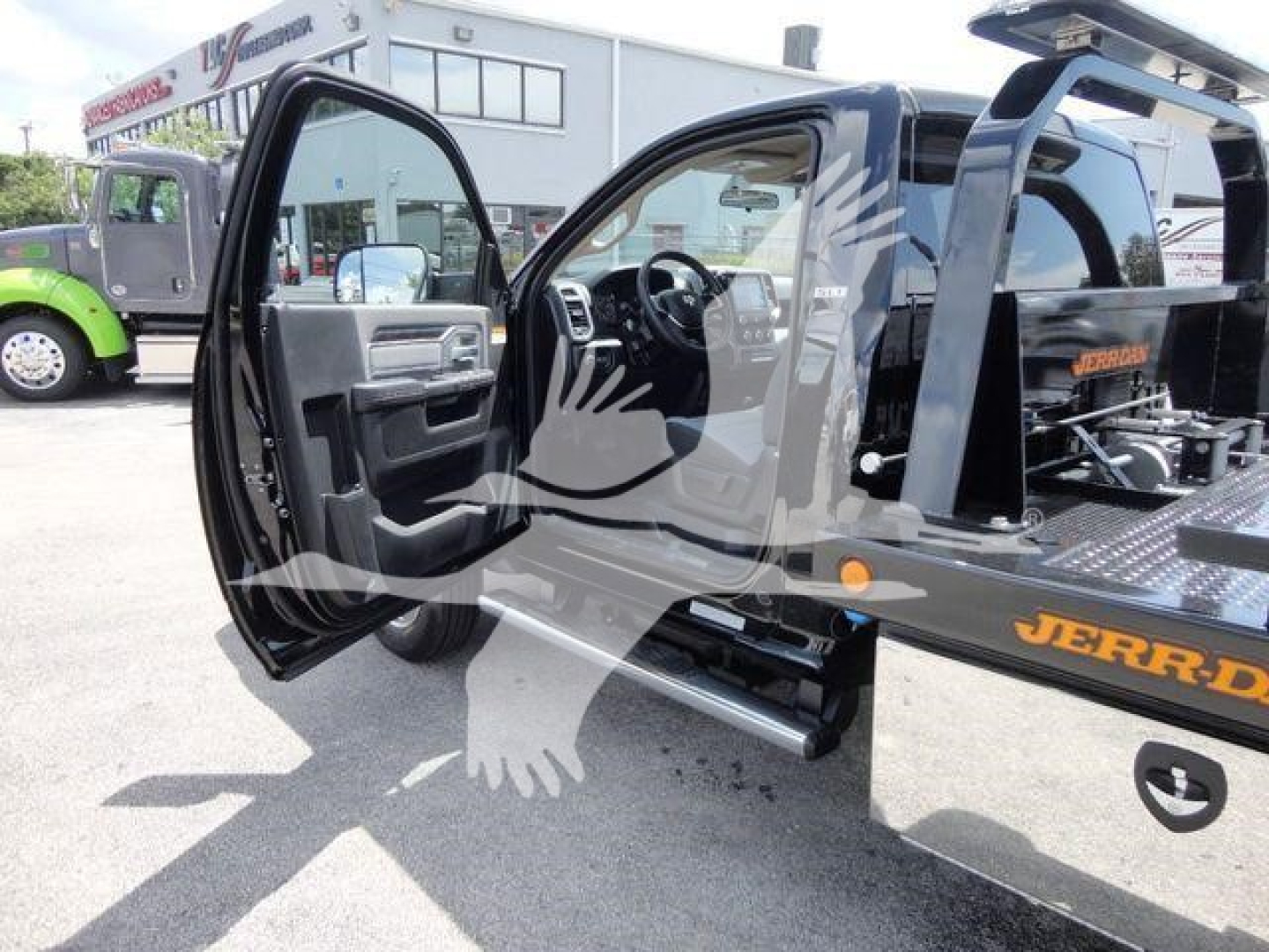 2024 Ram 5500 SLT rollback truck with driver door open showing interior and hydraulic rollback bed. Visible text includes JERR-DYNE on bed and a white storefront in background.