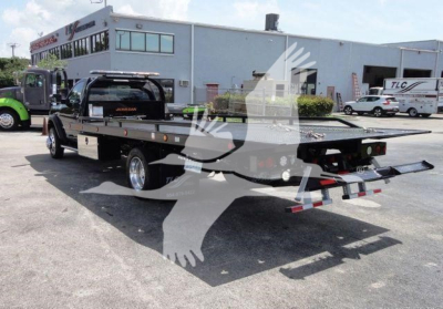 Flatbed tow truck in dealership lot showing Ram 5500 SLT in background and rollback bed with ramps.